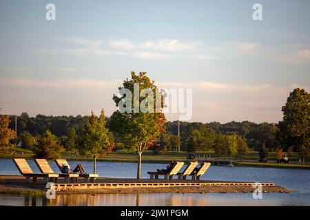 Persone che si rilassano su sedie di legno durante il tramonto al lago Patriot a Shelby Farms Park, Memphis, Tennessee. Il 31 agosto 2022. Foto Stock