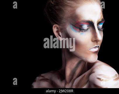 Tutto etereo. Studio shot di una giovane donna che posa con vernice sul suo viso isolato su nero. Foto Stock