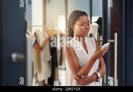 Prendersi cura di alcuni testi di lavoro. Un giovane imprenditore che utilizza un cellulare nel suo negozio. Foto Stock