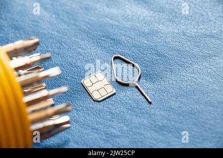 La scheda sim con pin e un set di cacciaviti si trovano su sfondo blu, riparazione e diagnostica di telefoni, assistenza e manutenzione Foto Stock