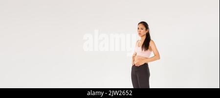 Tutta la lunghezza del upset e cupa ragazza asiatica di idoneità che prova a perdere il peso, toccando la pancia, cant vede i risultati dall'allenamento o dalla dieta, ritenente uneasy mentre Foto Stock