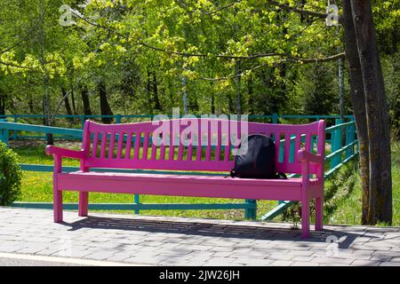 Una panchina rosa nel parco vicino al sentiero. Rubzak sulla panchina sotto l'albero. Foto Stock