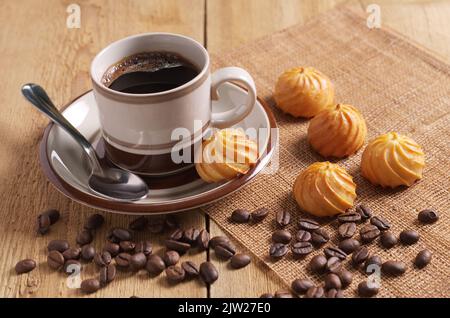 Tazza di caffè e piccole torte alla crema per la colazione su un tavolo di legno Foto Stock