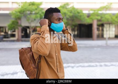 Uomo afroamericano in piedi fuori mettendo maschera di protezione Foto Stock