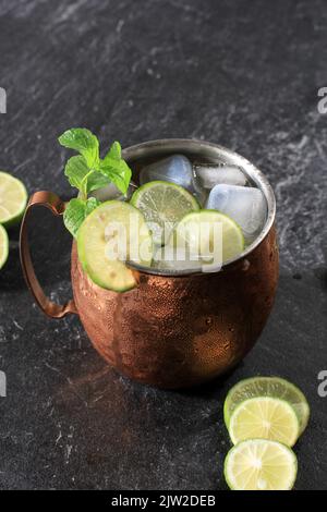 Cocktail alcolico Mule di Mosca in tazza di rame con ghiaccio, menta e limone a fette su sfondo di pietra nera. Primo piano Foto Stock