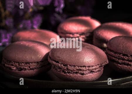 Deliziosi amaretti dolci di colore viola insieme sul tavolo illuminato al sole al mattino Foto Stock