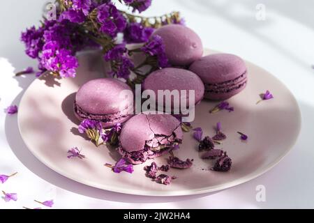 Mazzo di deliziosi amaretti viola serviti sul piatto vicino a fiori delicati su tavolo illuminato dal sole Foto Stock