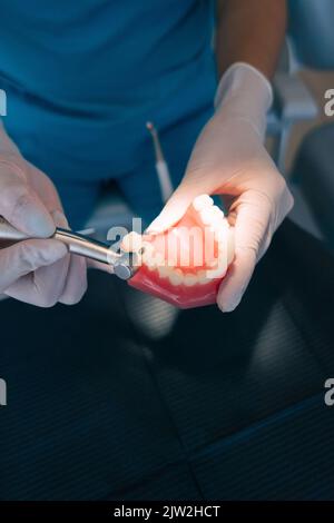 Vista dall'alto di un dentista femminile anonimo che utilizza un trapano dentale mentre si pratica il trattamento su una dentiera durante il lavoro in clinica moderna Foto Stock
