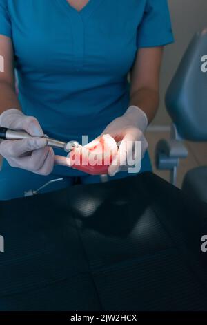 Vista dall'alto di un dentista femminile anonimo che utilizza un trapano dentale mentre si pratica il trattamento su una dentiera durante il lavoro in clinica moderna Foto Stock