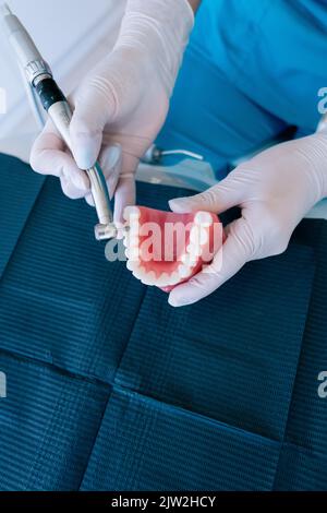 Vista dall'alto di un dentista femminile anonimo che utilizza un trapano dentale mentre si pratica il trattamento su una dentiera durante il lavoro in clinica moderna Foto Stock