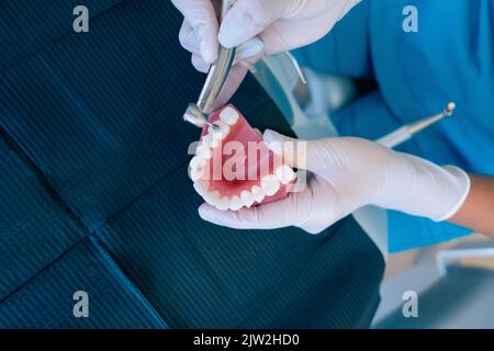 Vista dall'alto di un dentista femminile anonimo che utilizza un trapano dentale mentre si pratica il trattamento su una dentiera durante il lavoro in clinica moderna Foto Stock