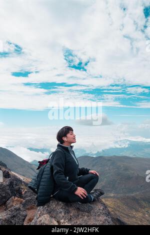 Vista laterale dell'escursionista femminile negli auricolari seduti sulla roccia a Padmasana, nelle Highlands, e ascoltando la meditazione mentre si rilassa e si fa yoga durante il trekking Foto Stock