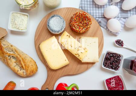 Formaggio di capra e di mucca assortito posto sul tagliere di legno vicino al pane e alle salse Foto Stock