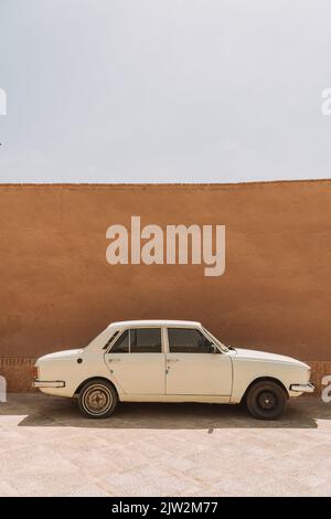Retro bianco berlina auto parcheggiata vicino al muro di cemento marrone sulla piazza nella giornata di sole a Yazd Foto Stock