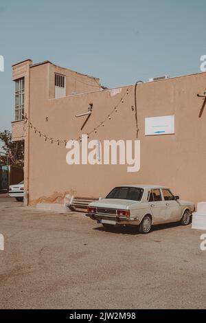 Bianco vecchio timer auto parcheggiata vicino a casa tipica su strada soleggiata in Iran il giorno d'estate contro il cielo blu Foto Stock