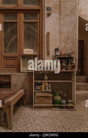 Vecchi armadietti di shabby con le bottiglie retrò e vasi collocati vicino a casa tradizionale stagionato in città di Iran il giorno d'estate Foto Stock