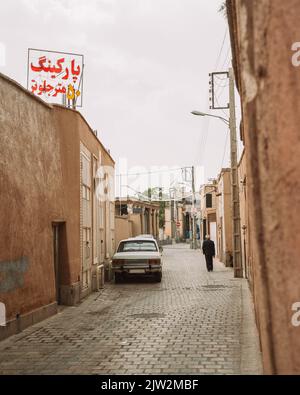 Strada lastricata con auto parcheggiata e cartello Parcheggio 10 metri più avanti sul tetto di vecchio edificio residenziale in Iran Foto Stock