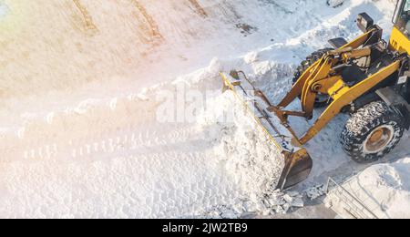 Un grande trattore arancione rimuove la neve dalla strada e libera il marciapiede. Pulizia e sgombero delle strade della città dalla neve in inverno. Rimozione della neve A. Foto Stock