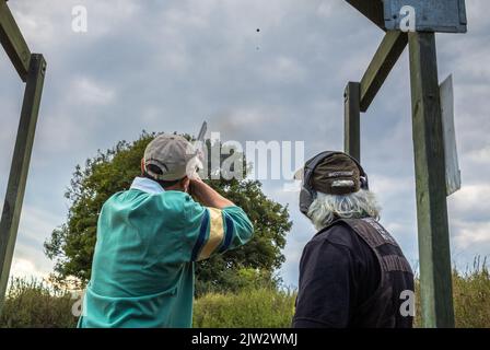 Un appassionato di armi colpisce un'argilla volante mentre un istruttore di tiro fornisce istruzioni durante il tiro al piattello al Southdown Gun Club, Findon, West Sussex Foto Stock