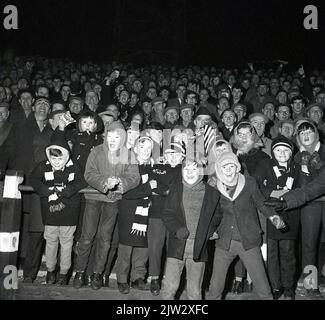 1960s, storico, tifosi di calcio, incontro serale, giovani entusiasti tifosi in piedi sulle terrazze, duffel cappotti e cappelli bobble per i giovani, non una replica camicia in vista! Foto Stock