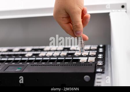 L'uomo lavora con le telecomunicazioni. Il consulente IT collega il cavo di rete allo switch del data center. Vista dal basso primo piano dell'interruttore manuale di un tecnico maschio Foto Stock