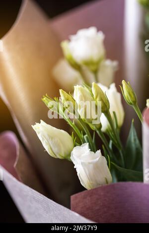 Primo piano di fiori di eustoma bianco in un bouquet avvolto in carta rosa. Concetto di congratulazioni per la Giornata internazionale della donna, il compleanno e la Madre D. Foto Stock