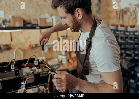 Sorridente uomo che ripara la macchina del caffè in un'officina Foto Stock