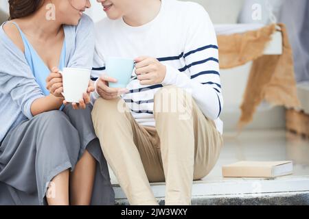 Immagine ritagliata di una giovane coppia seduta sulle scale con tazze da caffè Foto Stock