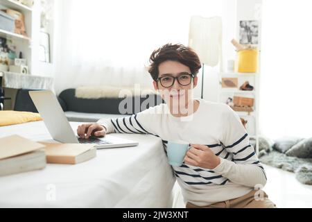 Ritratto dello studente con una tazza di caffè che lavora sul computer portatile Foto Stock