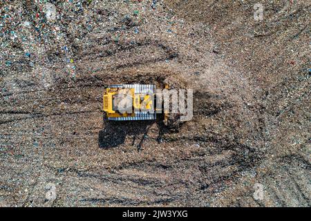 Una vista aerea di un bulldozer industriale che sposta i rifiuti domestici e i residui in un grande sito di discarica Foto Stock