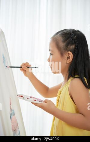 Piccola ragazza asiatica di talento concentrata sulla pittura Foto Stock