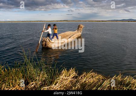 Isola di Uros, Lago Titicaca, perù, Sud America. I bambini navigano in una barca totora sul lago Titicaca. Il cambiamento climatico ha abbassato il livello del Lago Titica Foto Stock