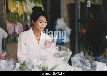 Attraente fiorista vitenamese concentrato sulla produzione di bouquet per il cliente Foto Stock