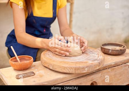 donna mani con pezzo di argilla sulla ruota di legno vasaio Foto Stock