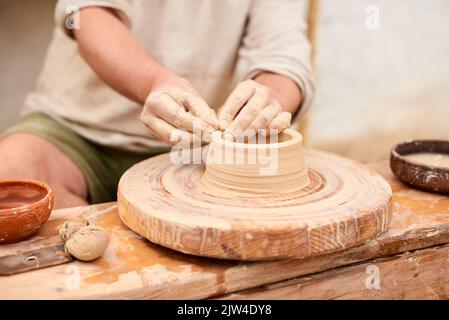 maestro artigiano maschile in camicia di lino chiaro scolpisce caraffa, ciotola o vaso di argilla Foto Stock