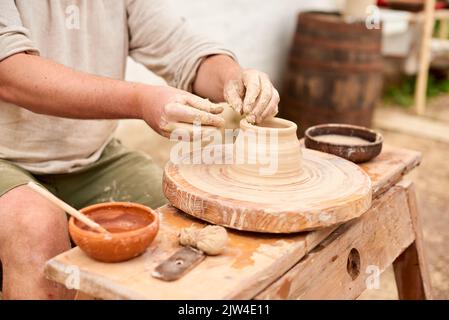 maestro artigiano maschile in camicia di lino chiaro scolpisce caraffa, ciotola o vaso di argilla in villaggio Foto Stock