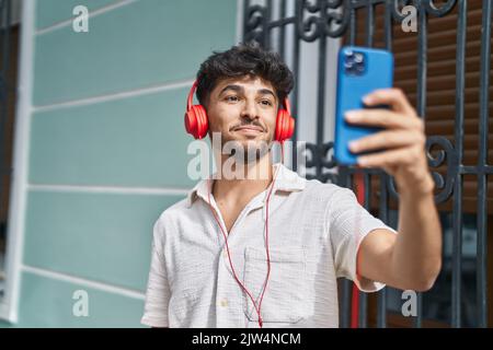 Giovane uomo arabo sorridente fiducioso di avere una videochiamata in strada Foto Stock