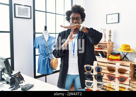 Giovane donna africana che lavora come manager in boutique retail facendo un gesto di time out con le mani, frustrata e faccia seria Foto Stock