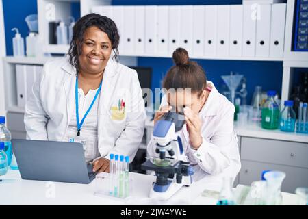 Madre e figlia scienziati che utilizzano microscopio e laptop che lavorano in laboratorio Foto Stock