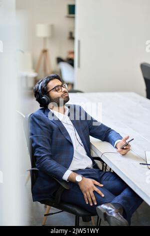 Uomo d'affari indiano rilassato indossando le cuffie seduti ad ascoltare musica mobile. Foto Stock