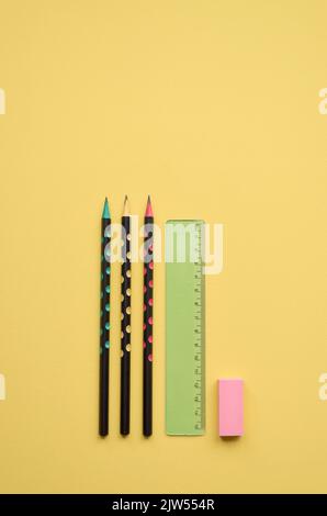 Matite, righello e gomma su sfondo giallo, piatto. Ritorno a scuola Foto Stock