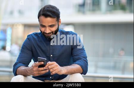 Uomo indiano di affari che usa il telefono delle cellule che siede sulla strada urbana della città. Foto Stock