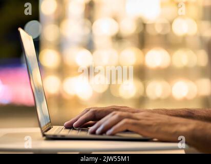 L'uomo d'affari ha le mani di digitare sulla tastiera del computer portatile sullo sfondo delle luci notturne. Foto Stock