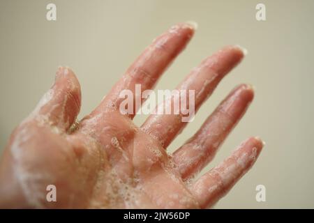 Bagnare la mano femmina con schiuma su sfondo beige. Vista laterale, primo piano. Foto Stock