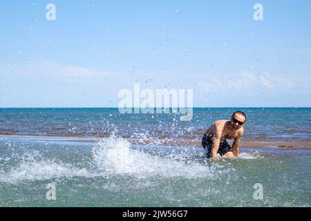 un uomo spruzza sull'acqua. ragazzo divertente in acqua. vacanze al mare Foto Stock