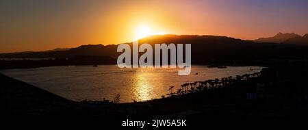 Vista aerea sul mare calmo e sulle montagne al tramonto. Spiaggia di sabbia con costa rocciosa e palme. Bellissimo paesaggio con orizzonti in estate sera raggi, Sharm El Sheikh, Egitto, banner. Foto Stock