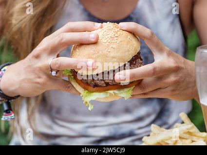 Mani che tengono un hamburger, su un tavolo da ristorante. Cibo delizioso e nutriente. Stile americano. Foto Stock