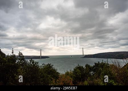 nave da carico che trasporta in mare su sfondo nuvoloso e ponte, commercio internazionale Foto Stock