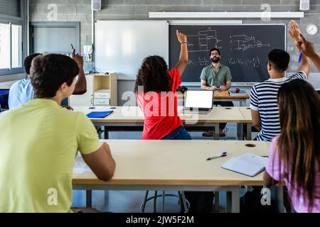 Gruppo di giovani studenti che si alzano le mani in classe in lezione Foto Stock