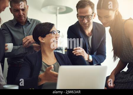 Presenta le idee migliori: Un gruppo di colleghi che discutono di qualcosa su un notebook durante una riunione. Foto Stock